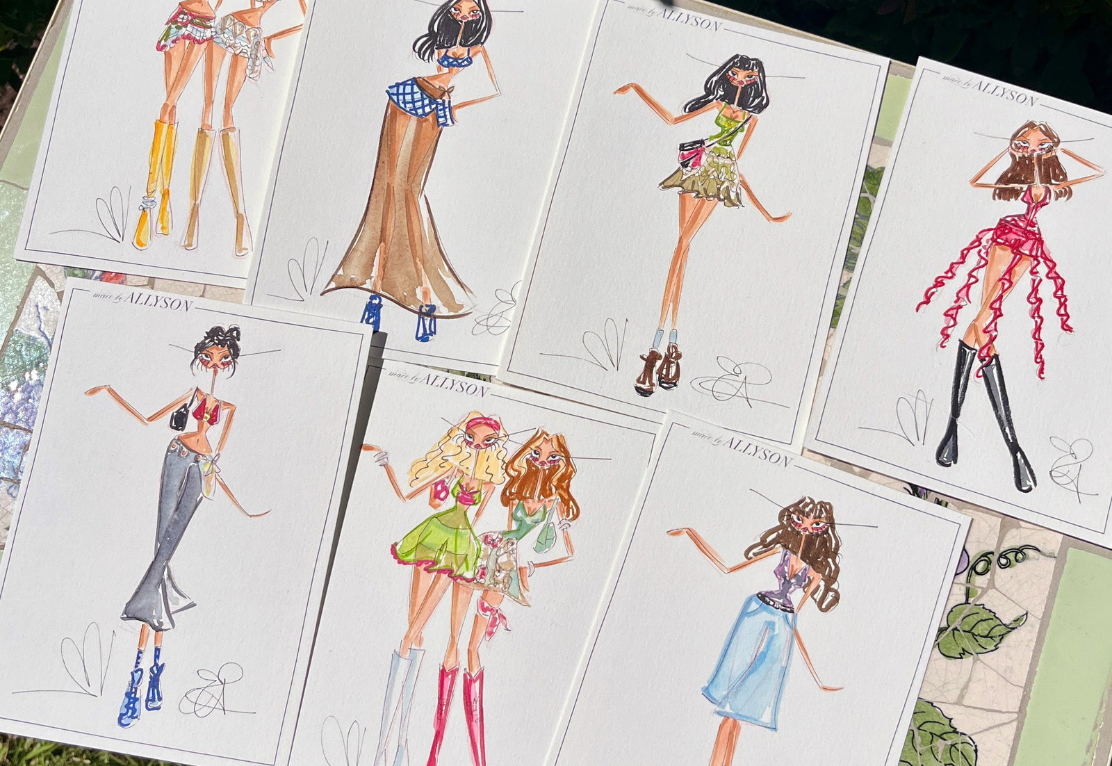 Illustrations of dolls in various outfits on a grassy surface